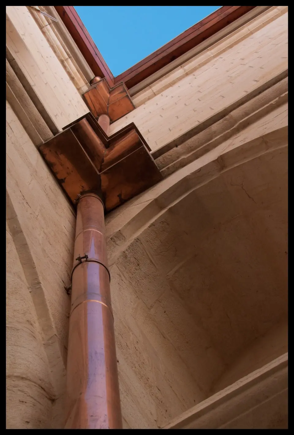 Gouttière et tuyau de descente en cuivre à l'angle d'un bâtiment en pierre.
